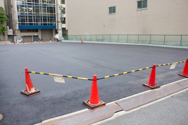 Turuncu güvenlik konileriyle çevrili, yeni asfaltlanmış boş otopark.