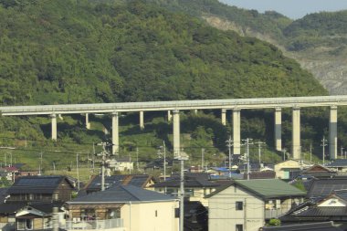 Yeşil yamaçlar boyunca uzanan yüksek otoban yerleşim yerlerinin çatıları üzerinde.