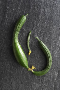 Siyah taş arka planda üç taze salatalık, üst manzara.