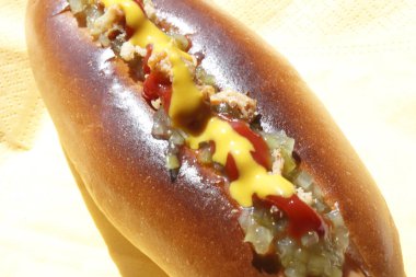 Yakın plan, parlak ışığın altında sosisli çöreği ve ketçap aromalı hardal görünüyor.