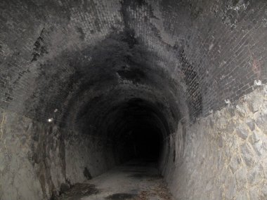 Engebeli taş duvarları ve karanlık bir girişi olan antik bir yeraltı tünelini araştırıyorum.