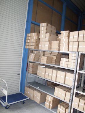 Raflarda düzgünce istiflenmiş karton kutularla dolu bir depo..