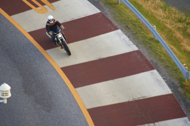 Bir şehrin asfalt yolunda motosiklet süren adam manzarası.