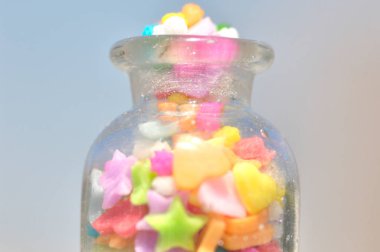 Açık arkaplanda cam kavanoz ve renkli şekerlerin yakın plan görüntüsü        