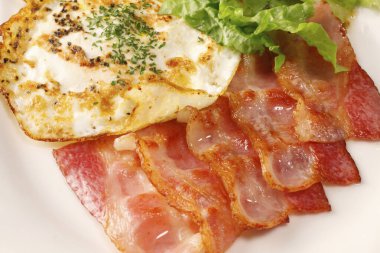 Domuz pastırmalı sahanda yumurta ve beyaz tabakta salata, yakın plan.