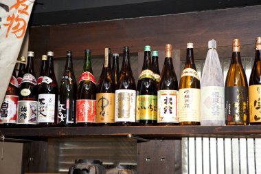 Çeşitli Japon sake şişeleri ahşap raflarda.