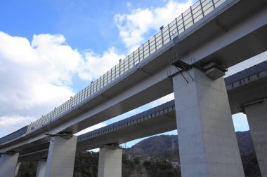 Yükseltilmiş otoyol, dağınık bulutlu, parlak mavi bir gökyüzünün altında manzaralı bir manzara boyunca uzanır.