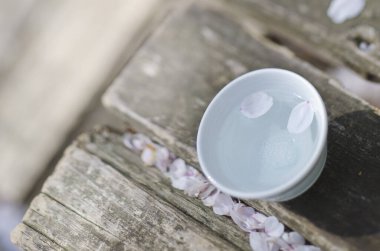 Tahta yüzeyinde sakura yaprakları olan bir fincan sake. Japonya 'da bahar mevsimi