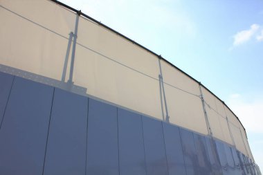 Kavisli modern bina dış görünüşü mavi gökyüzüne karşı güneş ışığını yansıtıyor