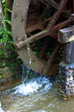 Eski ahşap su çarkı yosunlu taş duvarın yanında dönüyor