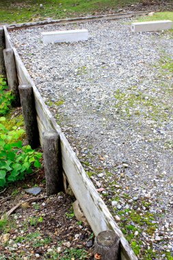 Etrafı ahşap sınırlarla çevrili boş çakıl bocce sahası.