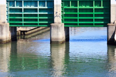 Sakin nehir suyunun üzerindeki güneş ışığını yansıtan yeşil metal kapakları