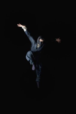 Siyah arka planda atlayan ninja kostümlü genç adam. 
