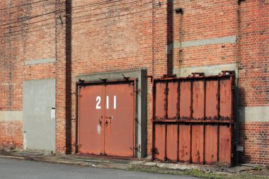 Metal kapılar ve konteynırlardan oluşan yıpranmış kırmızı tuğla duvar.