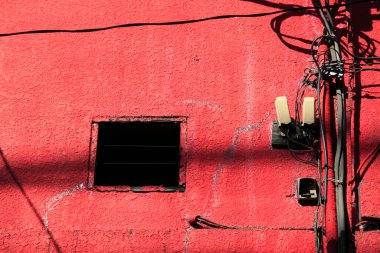 Yakınlarda birbirine dolanmış kablolarla dokulu kırmızı duvara kurulmuş siyah pencere.