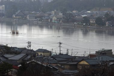 Sakin suların olduğu sakin nehir kenarı uzak evleri yansıtıyor.