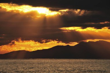 Manzaralı tepelerle deniz kıyısında güzel bir gün batımı.     