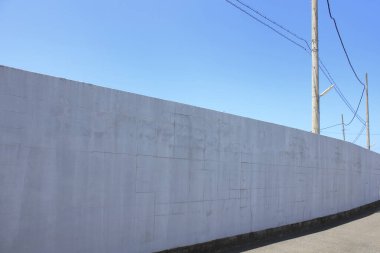 Açık gökyüzünün altında, boş cadde boyunca uzanan uzun beton duvar.