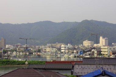 Turnaların, çatıların ve puslu yeşil dağların bulunduğu uzak şehir manzarası