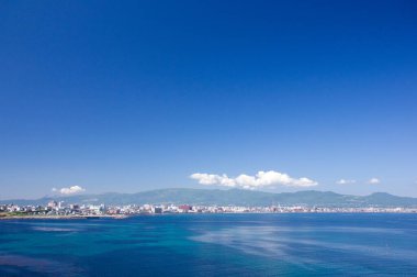 Sakin mavi deniz manzarası ve ufukta tepeler olan kıyı kasabası.