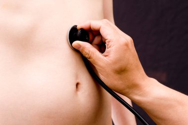 Steteskoplu bir doktor çıplak gövdeli bir adamı muayene ediyor.