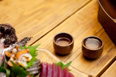 İki seramik sake bardağının yanında çeşit çeşit saşimi.