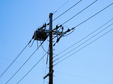 Mavi gökyüzüne karşı yüksek voltajlı elektrik hatlarının düşük açılı görüntüsü  