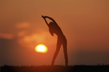 Gün batımında yoga yapan genç bir kadının silueti.