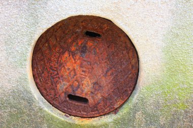 Beton yüzeyde paslı rögar kapağı.