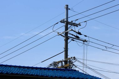 Açık mavi gökyüzüne karşı elektrik kablolarını destekleyen elektrik direği