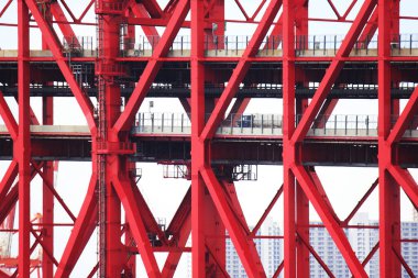 Parlak kırmızı çelik yapı gündüz saatlerinde şehir ortamında karmaşık tasarım ve mühendislik gösteriyor