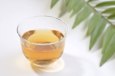 Beyaz arka planda yaprakları olan bir bardak taze çay.