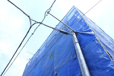 Gökyüzüne karşı yüksek binayı kaplayan mavi inşaat brandası