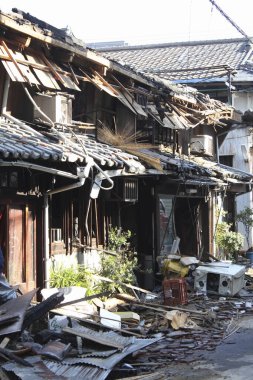 Hasarlı geleneksel ahşap ev çökmüş çatıyı ve dağınık enkazı gösteriyor.