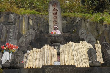 Etrafı ahşap adaklarla çevrili bir heykel içeren taş tapınak.