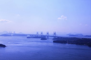 Uzaktan asma köprü bulutlu gökyüzünün altında sakin mavi su yayıyor