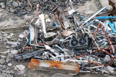 Kırık elektronik aletler ve paslı borular dahil etrafa saçılmış metal enkazı.