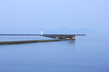 Sakin mavi deniz bulutlu gökyüzünün altında beton iskeleyle buluşuyor.