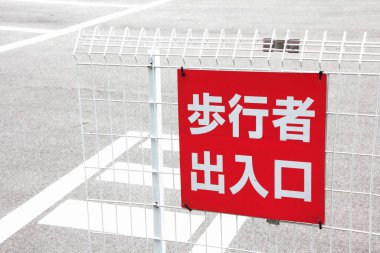 Kırmızı Japon tabelası yaya geçidinin yanındaki beyaz metal çitlerde asılı.