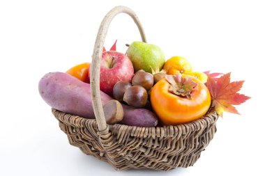 Tatlı patates, elma, mandalina, armut, taze hurma, kestane ve akçaağaç yaprakları beyaz arka planda izole edilmiş sepette.