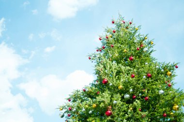 Mavi gökyüzüne karşı parlak mücevherleri olan şenlikli Noel ağacının alçak açılı görüntüsü   