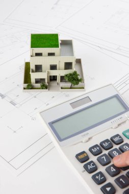 Mimarın eli, ev modeli ve planlarıyla hesap makinesi kullanıyor.    