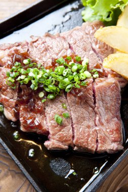 Bir biftek ve siyah tabakta biraz sebze.