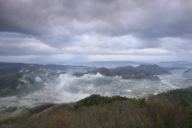 Şehir manzarası, dağlar ve deniz fırtınalı bulutlar altında. 