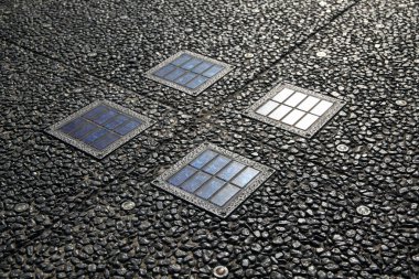 Kalıplı taş kaldırıma yerleştirilmiş dört kare cam panel.