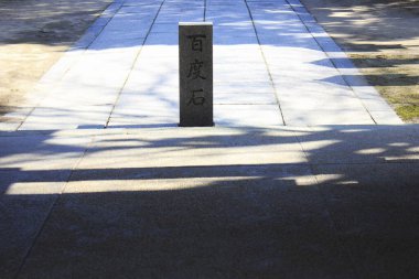 Güneşli yolda duran taş işaret keskin gölgeler bırakıyor.