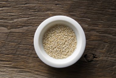 Tahta arka planda kinoa taneleriyle dolu küçük beyaz kase.