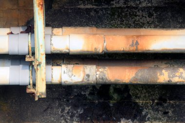 Paslı endüstriyel borular yıpranmış duvar yüzeyine yatay olarak akıyor