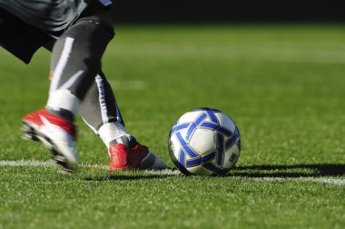 Bir futbolcu sahada futbol topunu tekmeliyor.