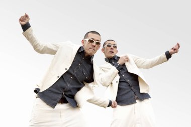 Beyaz takım elbiseli ve güneş gözlüklü iki Asyalı beyaz stüdyoda poz veriyor. 